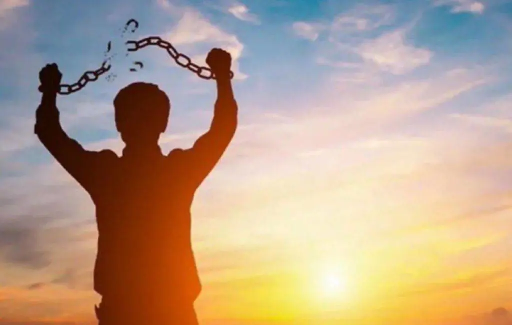 Image of person breaking hand chains with sunset in background
