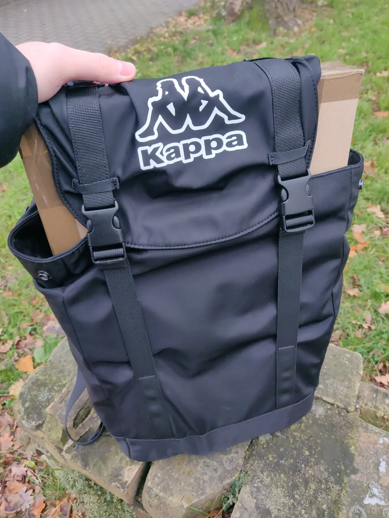 Image showing me holding a backpack, which is overfilled with one long brown box, backpack is keeping it inside by the strips