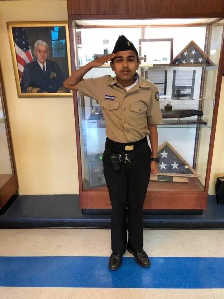 Guy in an uniform standing and saluting in front of some army stuff